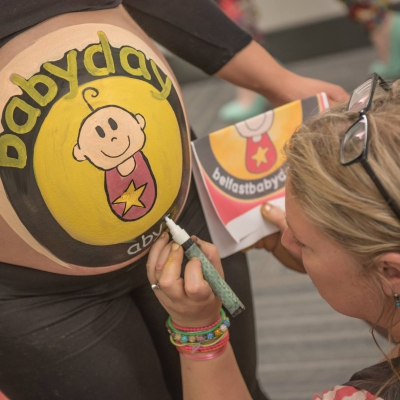Preganant woman getting belly painted with BabyDay logo